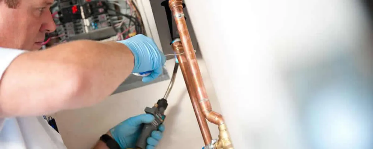 Water heater repair technician testing copper pipe connections and controls in Wellesley, MA